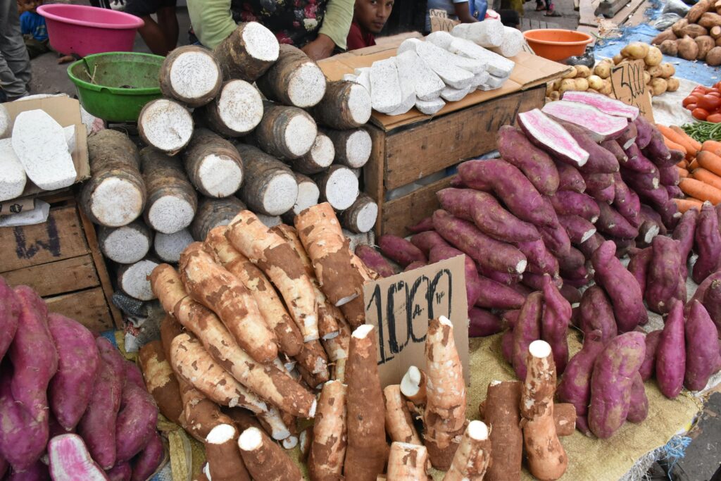 Fresh yams and cassava on display at an outdoor market stall, showcasing a variety of root vegetables.