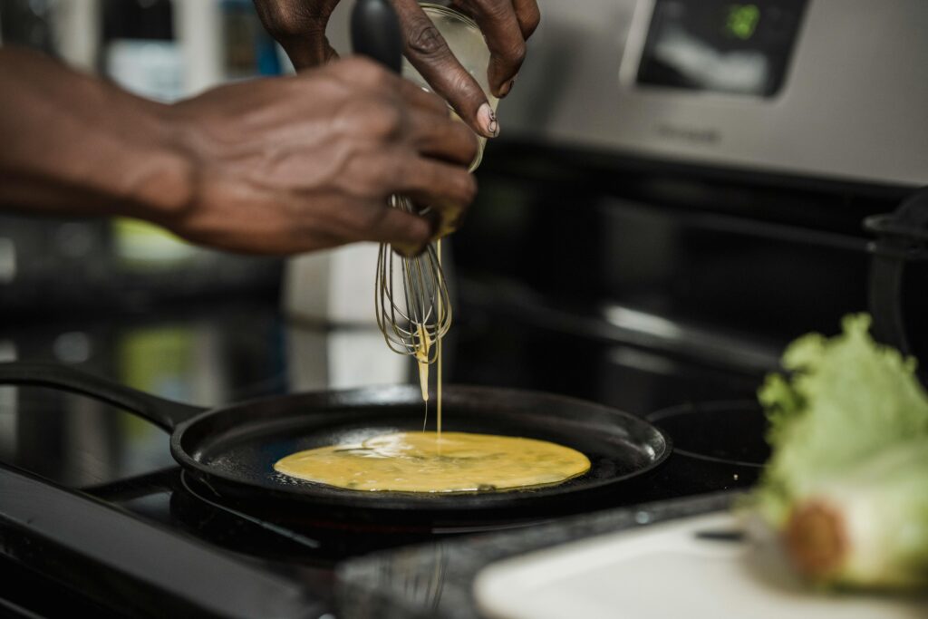 Close-up of a person pouring egg mix into a pan on a stove for breakfast.