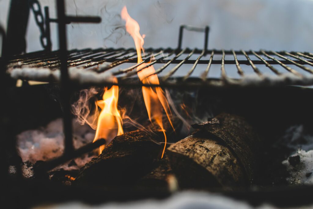 Close-up view of firewood burning in a fire pit with a metal grill above, outdoor setting.